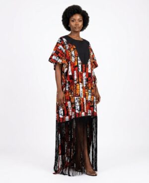 Woman wearing a floor-length African print kaftan dress with orange abstract patterns and black fringe hem.