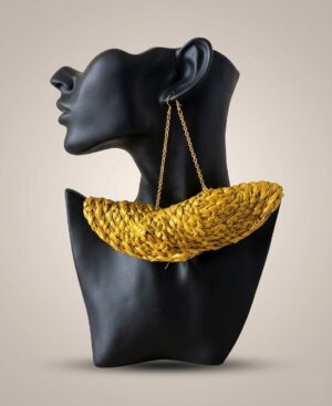 Handwoven oversized mustard yellow crescent Statement Raffia Earring hanging from gold chains on a matte black mannequin bust.