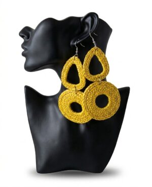 A pair of oversized handmade woven statement drop raffia earrings in vibrant mustard yellow displayed on a black mannequin bust.