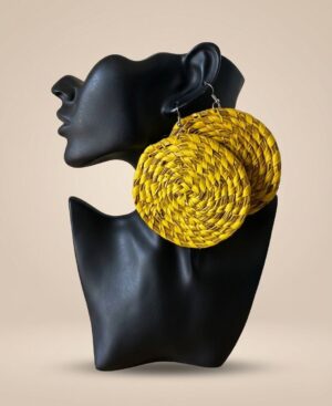 A pair of oversized, vibrant yellow woven straw circular statement earrings displayed on a matte black female display bust against a beige background.