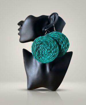 Pair of large, circular woven statement earrings in teal green displayed on a black female bust mannequin against a gray background.
