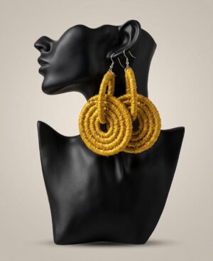 A pair of oversized mustard yellow woven fiber statement earrings displayed on a matte black mannequin bust.