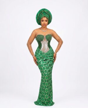 Woman wearing a luxury emerald green beaded lace Aso Ebi gown with a matching pleated Gele headwrap.