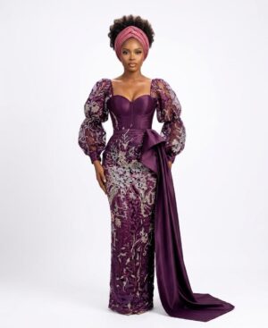 Make a grand entrance in this luxurious deep purple lace gown. Featuring a structured corset bodice, romantic sheer puff sleeves, and a dramatic satin side drape, this mermaid-style dress combines traditional African elegance with modern high-fashion tailoring. Perfect for weddings and formal galas.