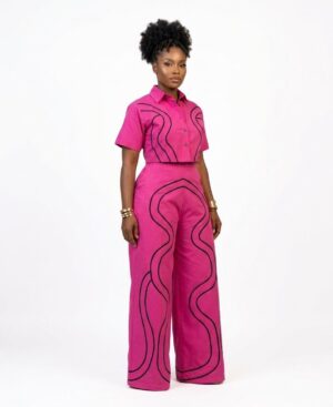 Woman wearing a fuchsia pink two-piece set with black wavy line embroidery, including a cropped shirt and wide-leg trousers.