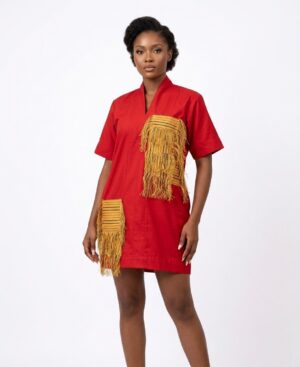 Woman wearing a short red shift dress with large mustard yellow fringed pockets featuring woven African patterns.