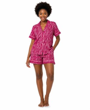 Smiling woman wearing a bright fuchsia and pink adire-inspired striped short pajama set with contrast piping and side pockets.