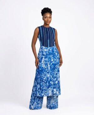 A woman wearing a blue hand-dyed Adire sleeveless tunic with a striped chest panel and matching wide-leg trousers against a white background.